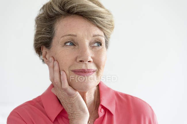 Primer plano de la mujer mayor feliz pensando con la mano en la cara - foto de stock