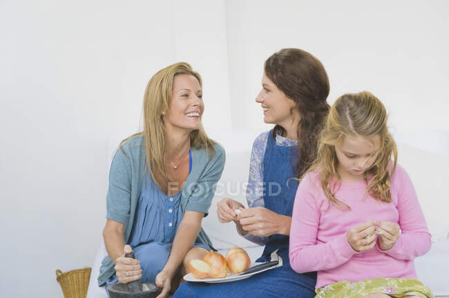 Dos mujeres preparando comida con una chica en casa - foto de stock