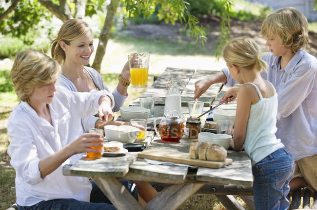 Happy mother and kids having food on summer backyard — Stock Photo