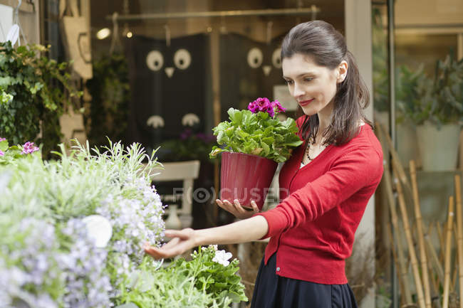 Donna in possesso di pianta in vaso e guardando i fiori nel negozio di fiori — Foto stock