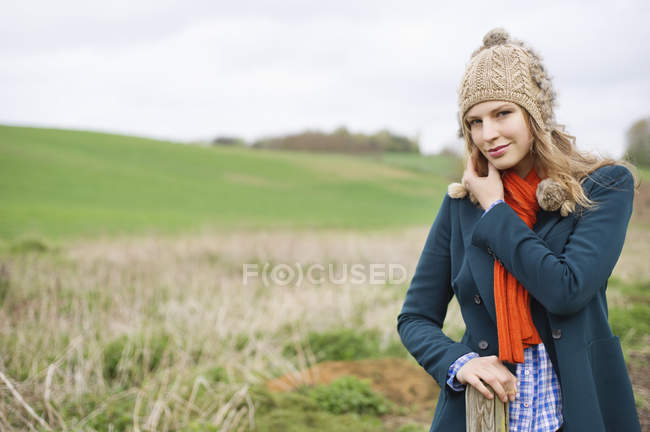 Retrato de mulher em cachecol vermelho e chapéu de lã em pé no campo — Fotografia de Stock