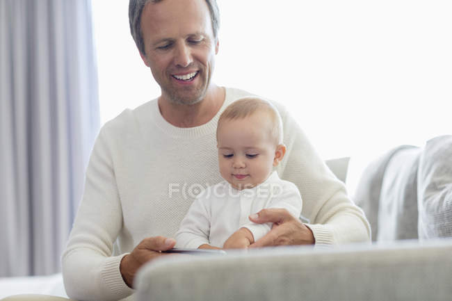 Feliz padre e hija jugando con el teléfono móvil en el sofá - foto de stock