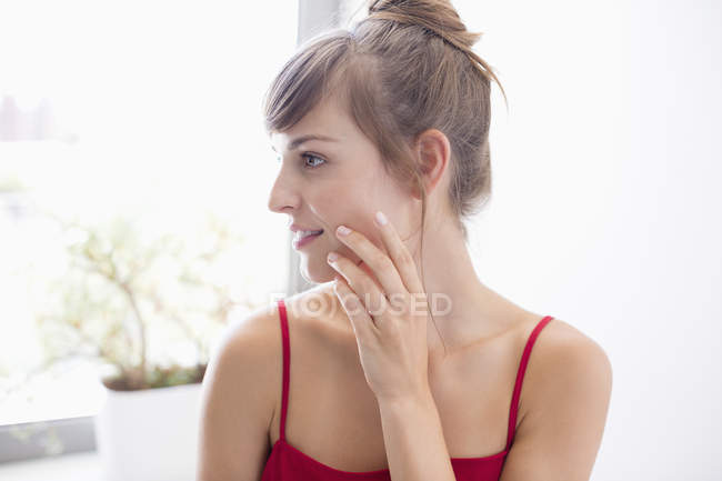 Mujer joven aplicando crema hidratante en la cara en el baño - foto de stock