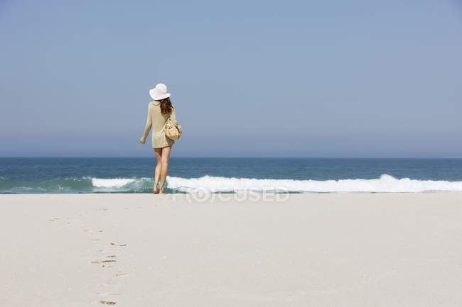 Vista posteriore della donna in cappello in piedi sulla spiaggia sabbiosa — Foto stock