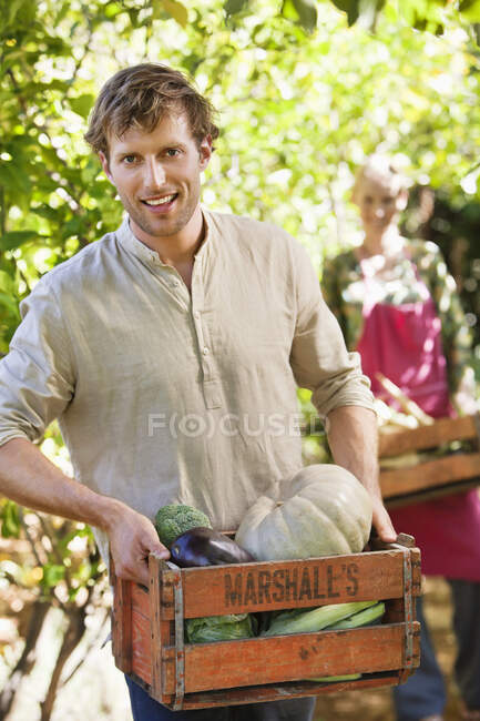 Усміхнений чоловік тримає ящик з овочами — стокове фото