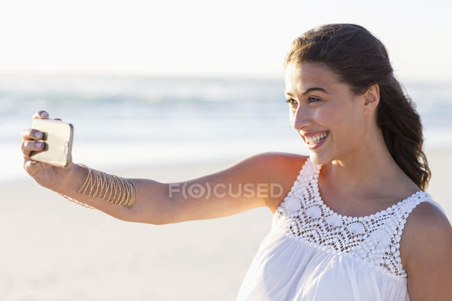 Feliz joven mujer tomando selfie con teléfono inteligente en la playa - foto de stock