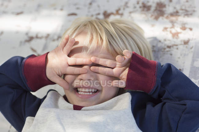 Menino brincalhão deitado e cobrindo os olhos com as mãos — Fotografia de Stock