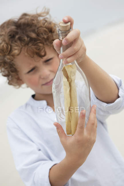 Мальчик смотрит на сообщение в бутылке на пляже — стоковое фото