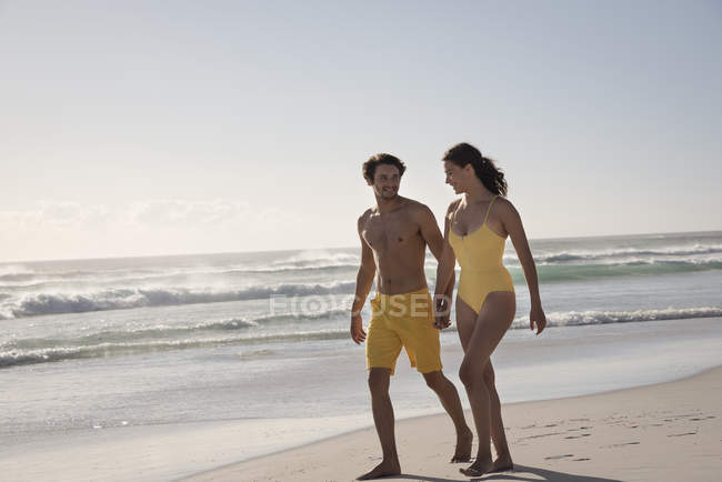 Glückliches junges Paar geht Händchen haltend am Strand spazieren — Stockfoto