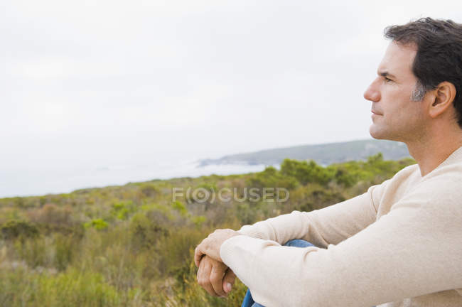 Uomo premuroso seduto sulla costa e guardando la vista sul mare — Foto stock