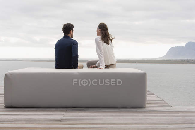Visão traseira do casal sentado no otomano no lago e olhando para a vista — Fotografia de Stock