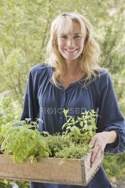 Ritratto di giovane donna bionda che trasporta cassa di piante in giardino — Foto stock