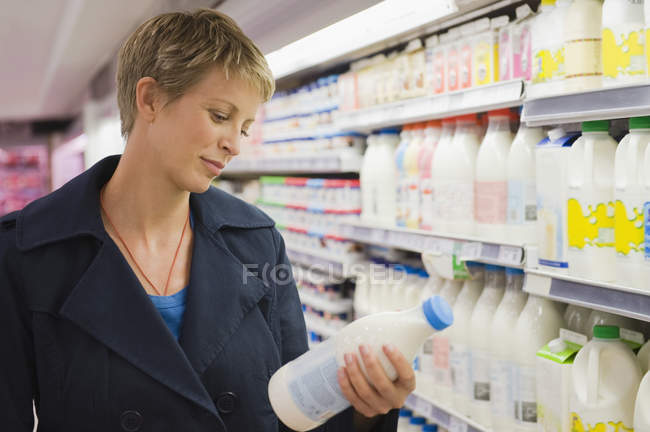 Woman checking bottle of milk while shopping in a supermarket — Stock Photo