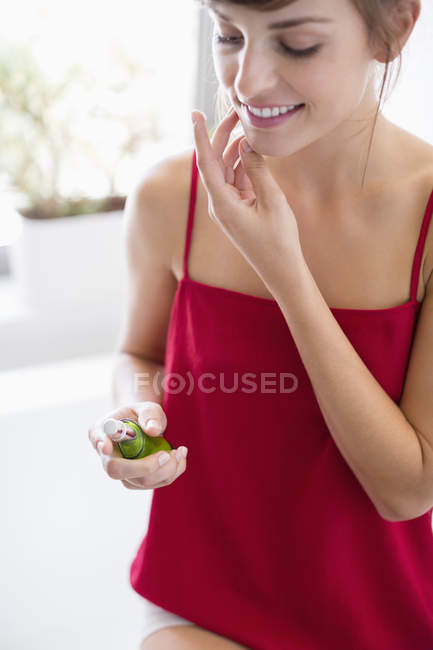 Lächelnde junge Frau trägt Feuchtigkeitscreme auf Gesicht im Badezimmer auf — Stockfoto