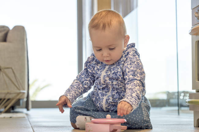Крупный план малышки, играющей с игрушкой на полу дома — стоковое фото