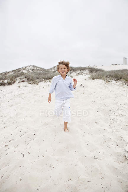 Lindo chico sonriente corriendo en la playa de arena - foto de stock
