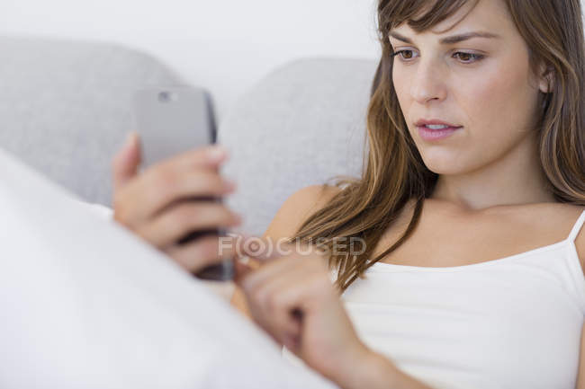 Mulher jovem mensagens com telefone celular na cama — Fotografia de Stock