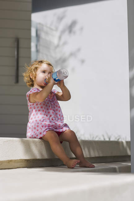 Babymädchen trinkt Wasser aus Flasche auf sonniger Veranda — Stockfoto