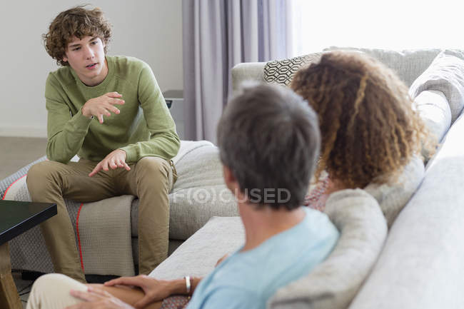 Мальчик разговаривает с родителями, сидя на диване в гостиной дома — стоковое фото