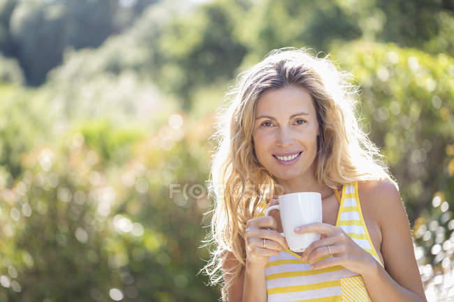 Портрет усміхненої жінки, що має чашку кави в літньому саду — стокове фото
