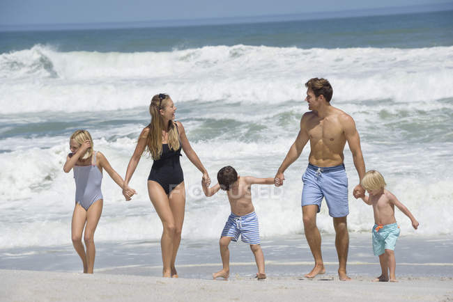 Счастливая семья гуляет по пляжу держа за руки — стоковое фото