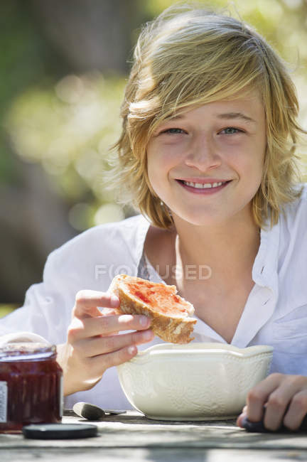 Retrato de un adolescente comiendo pan con mermelada al aire libre - foto de stock