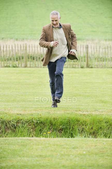 Homem maduro correndo em campo verde — Fotografia de Stock
