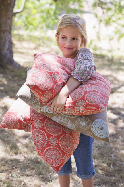 Retrato de menina sorridente carregando travesseiros ao ar livre — Fotografia de Stock