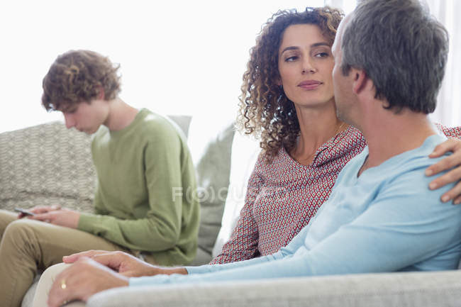 Пара сидить на дивані і розмовляє з сином, використовуючи мобільний телефон на фоні у вітальні вдома — стокове фото