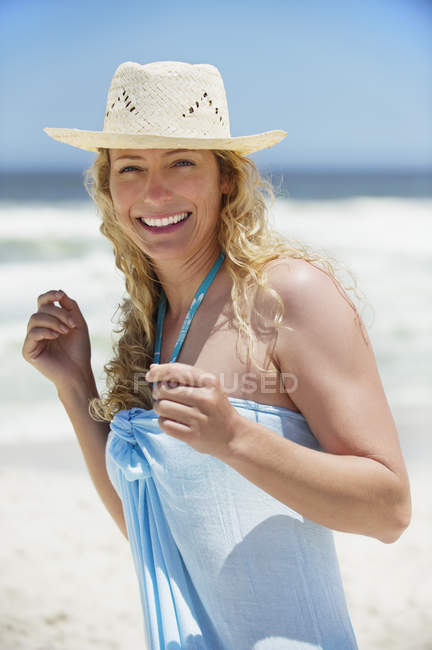 Retrato de mulher sorrindo usando chapéu de sol em pé na praia — Fotografia de Stock