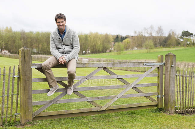 Homme assis sur une clôture en bois dans le champ — Photo de stock