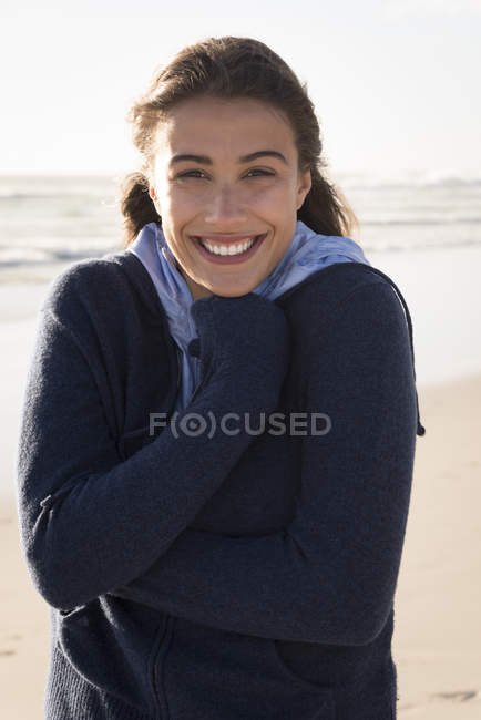 Portrait de jeune femme charmante à capuche chaude debout sur la plage — Photo de stock