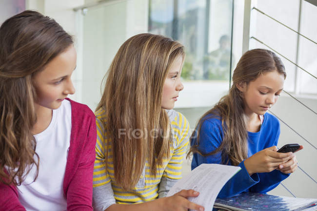 Girl using mobile phone while female pupils looking at her — Stock Photo