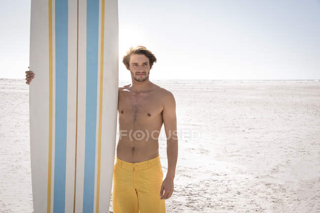 Glücklicher junger Mann mit Surfbrett am Strand — Stockfoto