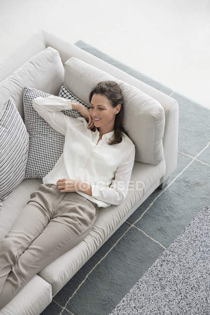 Happy mature woman lying on couch at home — Stock Photo