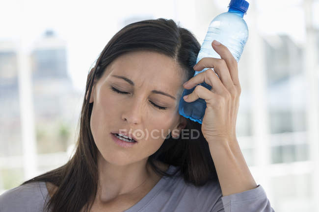 Mulher segurando garrafa de água na testa — Fotografia de Stock