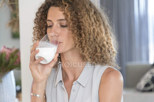 Primer plano de la mujer que bebe leche de vidrio en casa - foto de stock