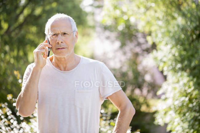 Старший чоловік розмовляє по мобільному телефону в саду — стокове фото