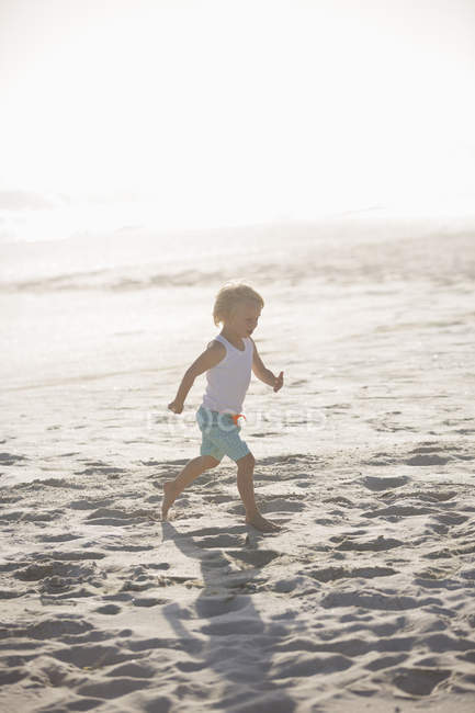 Menino correndo na praia de areia sob a luz do sol — Fotografia de Stock