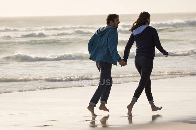 Felice a piedi nudi giovane coppia che corre sulla spiaggia al tramonto in autunno — Foto stock