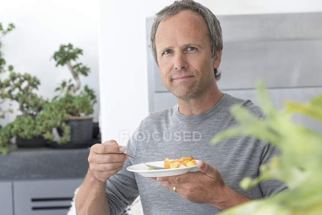 Portrait of mature man eating fruit salad in kitchen — Stock Photo