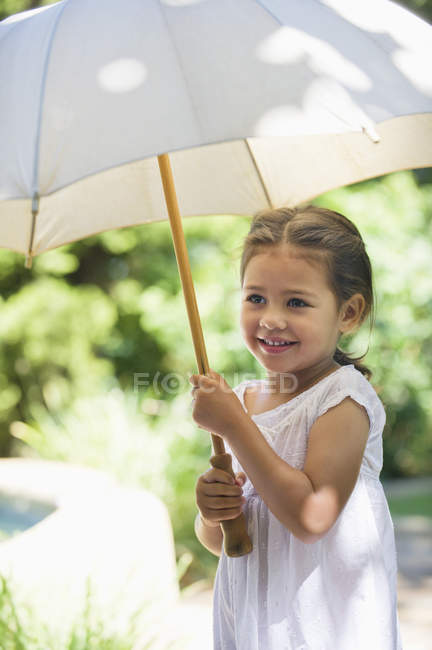 Cute little girl holding umbrella in sunny garden — Stock Photo