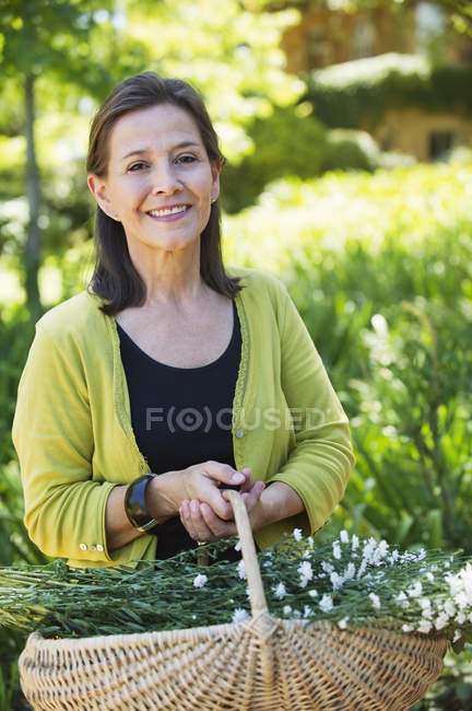 Portrait of a woman holding basket of flowers outdoors — Stock Photo