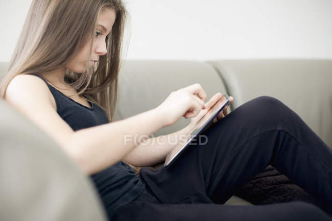 Adolescente ragazza utilizzando tablet digitale sul divano a casa — Foto stock