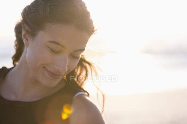 Усміхнена молода жінка стоїть на пляжі на сонячному світлі — стокове фото