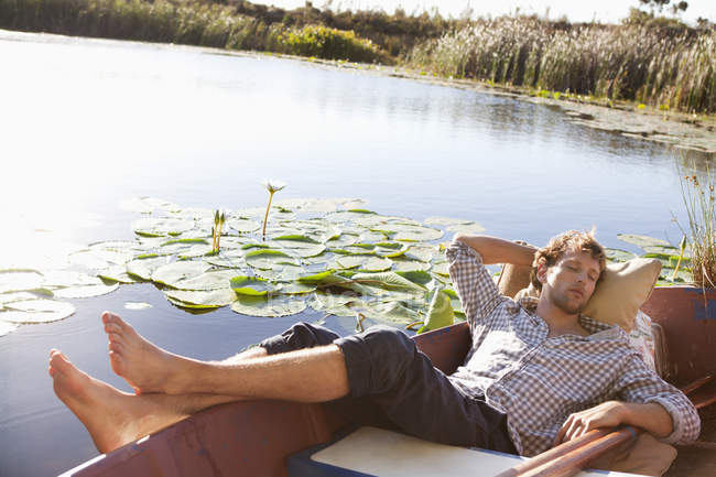 Relaxed young man sleeping in boat on lake in countryside — Stock Photo