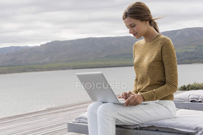 Улыбающаяся молодая женщина с ноутбука на берегу озера — стоковое фото