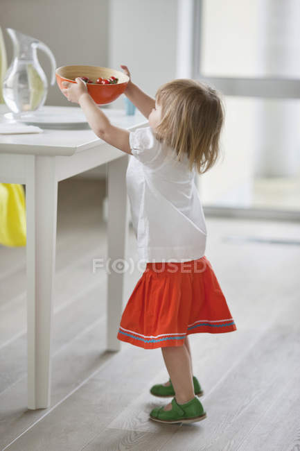 Chica poniendo tazón de comida en la mesa en casa - foto de stock