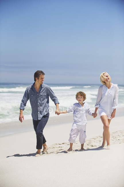 Niño caminando con sus padres en la playa - foto de stock