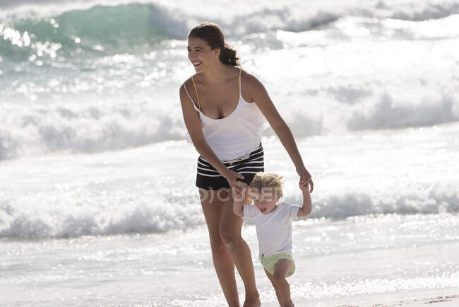 Счастливая мать со своим маленьким сыном, гуляющим по пляжу — стоковое фото